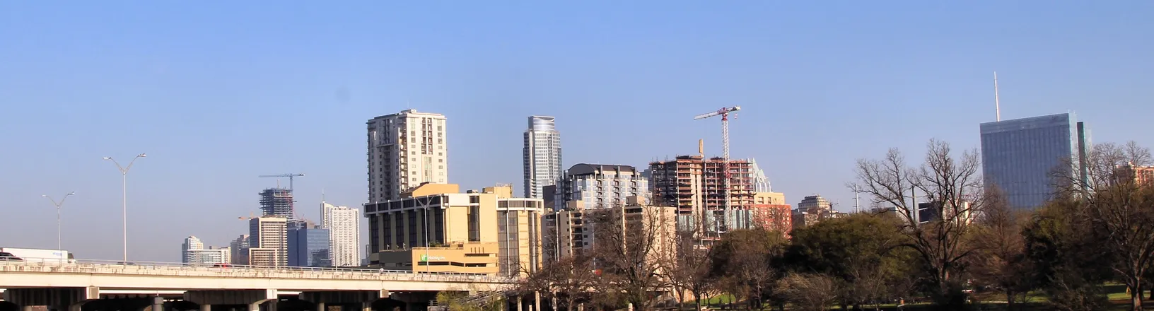 Downtown Austin seen across the water, with glass towers rising behind a tree-lined bank.