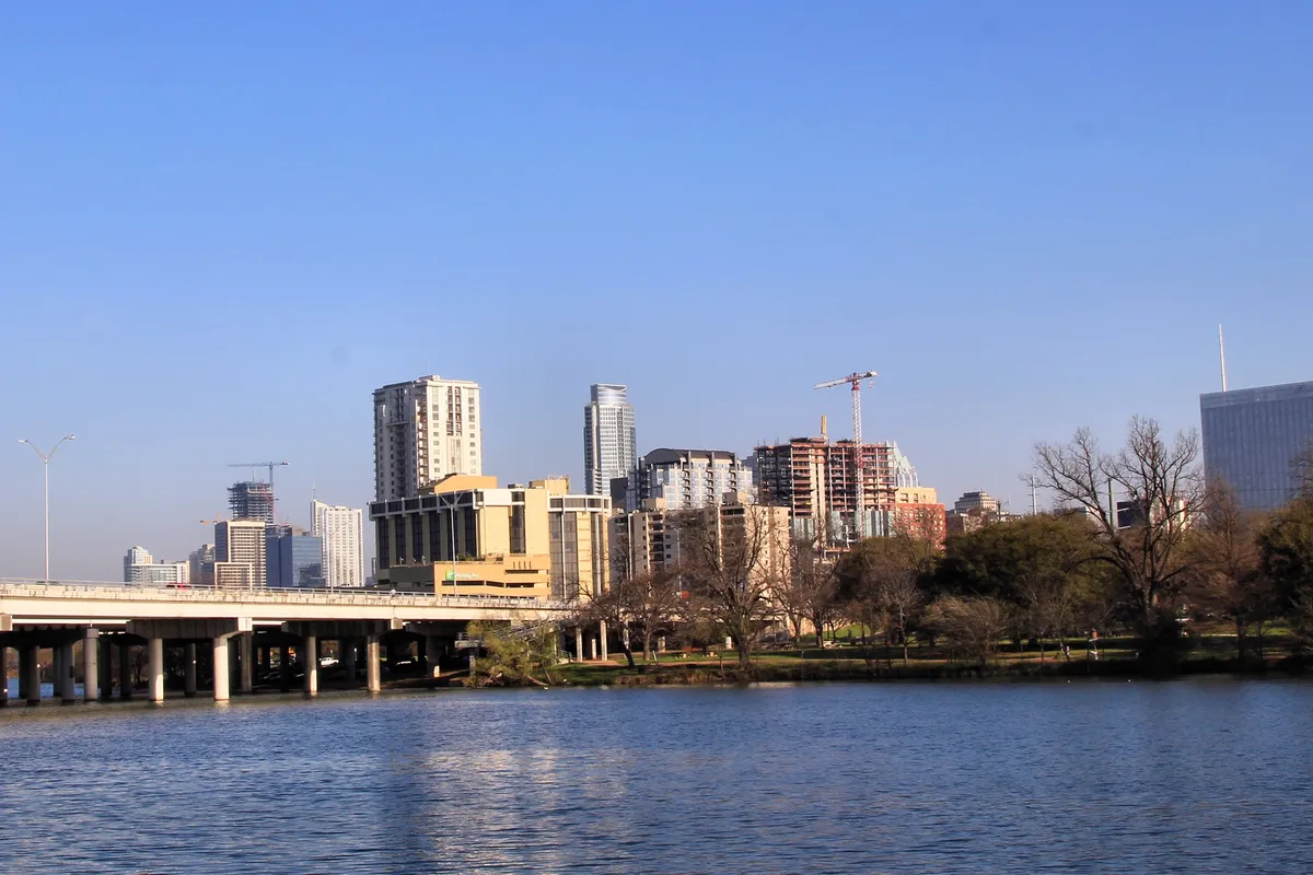 Downtown Austin seen across the water, with glass towers rising behind a tree-lined bank.